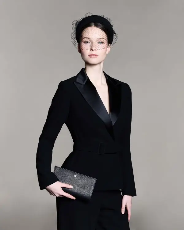 Woman wearing a black headband with a veil over her eyes and carrying a black leather bag.
