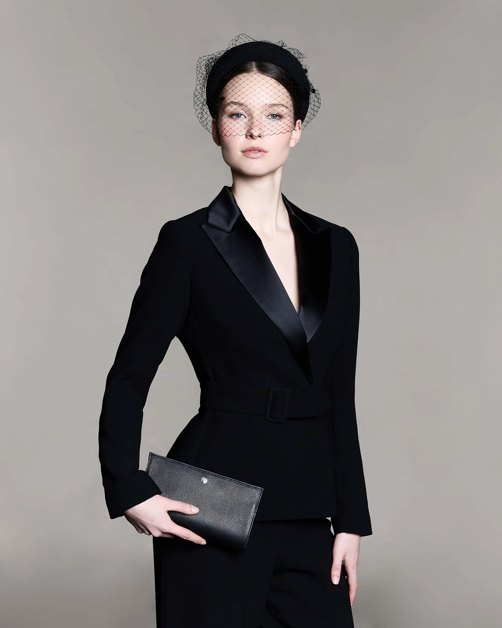 Woman wearing a black headband with a veil over her eyes and carrying a black leather bag.