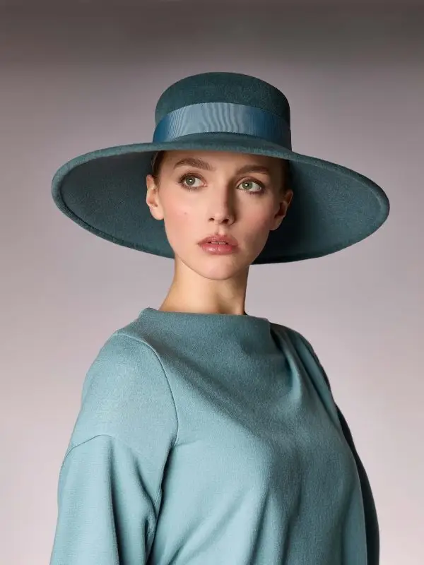 Woman wearing the green duck-shaped winter capeline hat of Hepburn