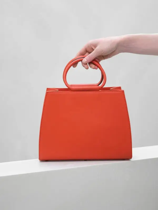 A hand placing the everyday Bella orange leather handbag accessory
