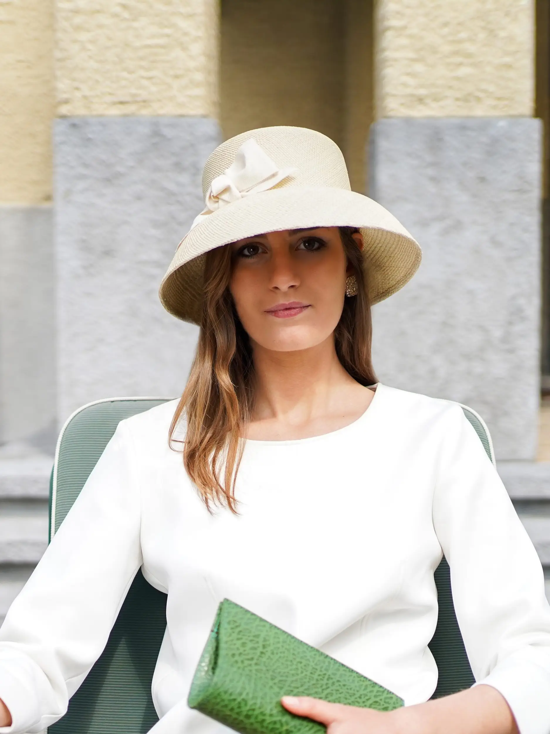 Woman wearing the Audrey cloche hat in natural Panama and the Colette clutch bag in green leather