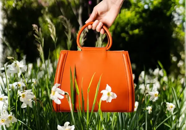 Orange leather bag in daisies held by a woman's hand
