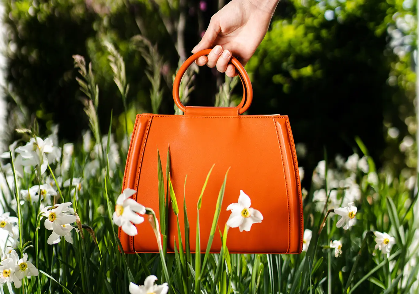 Orange leather bag in daisies held by a woman's hand