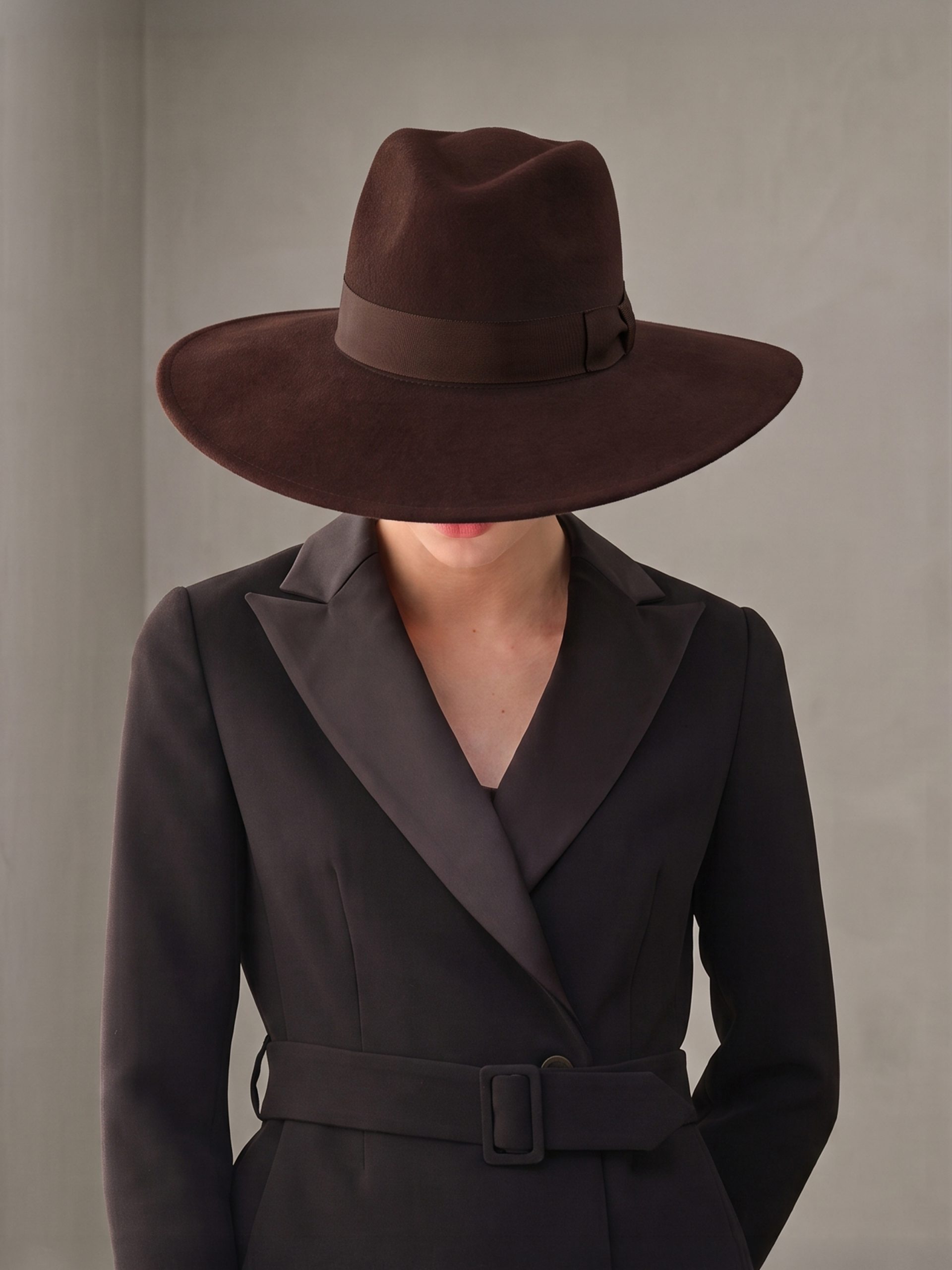 Woman with her head bowed wearing the Felicia brown felt fedora hat by Maison Fabienne Delvigne1