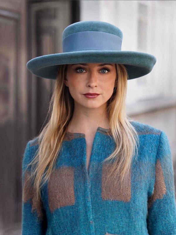 Woman wearing the Hidalgo cap with a green canard hat with a matching coat - Maison Fabienne Delvigne