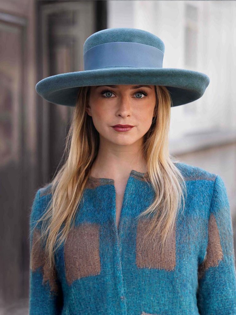Woman wearing the Hidalgo cap with a green canard hat with a matching coat - Maison Fabienne Delvigne